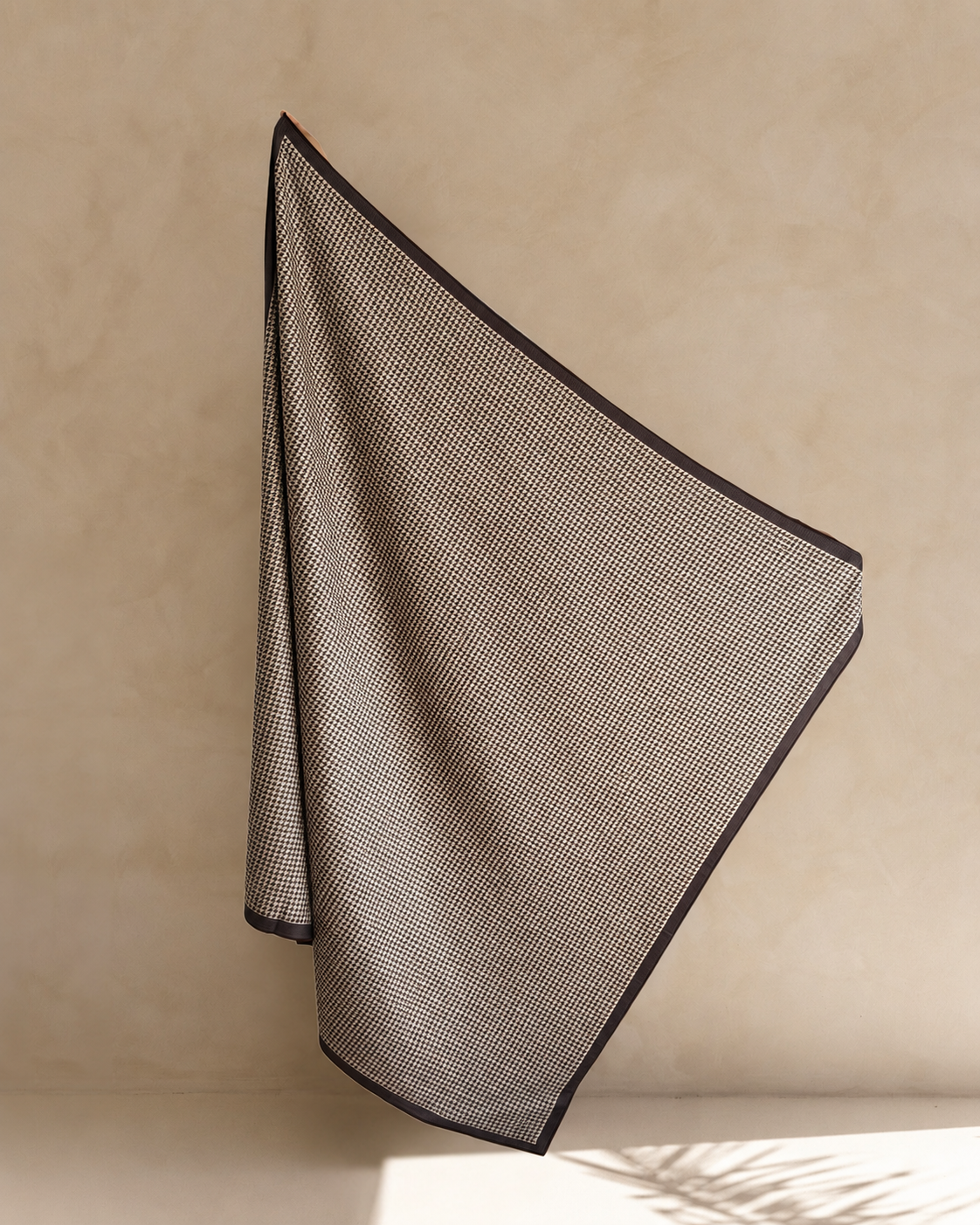 Espresso extra large sand free beach towel for two, chocolate brown houndstooth with a dark border, hanging against a sandstone wall