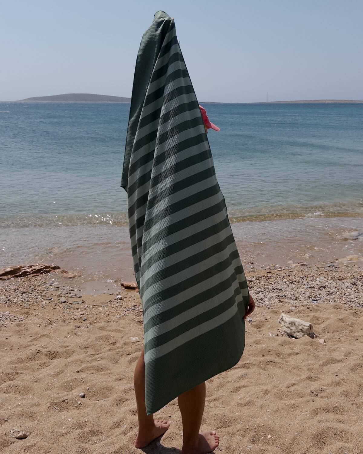 Person holding a green and light green striped towel on a beach with ocean in the background