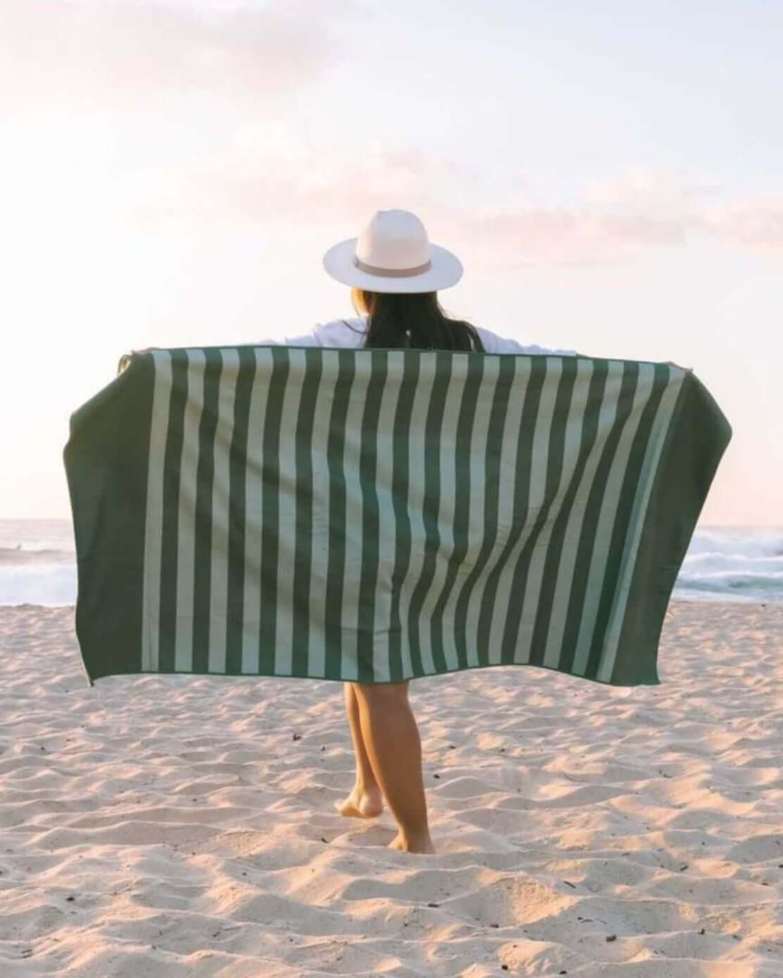 Person on a beach with a green and olive striped towel draped over them