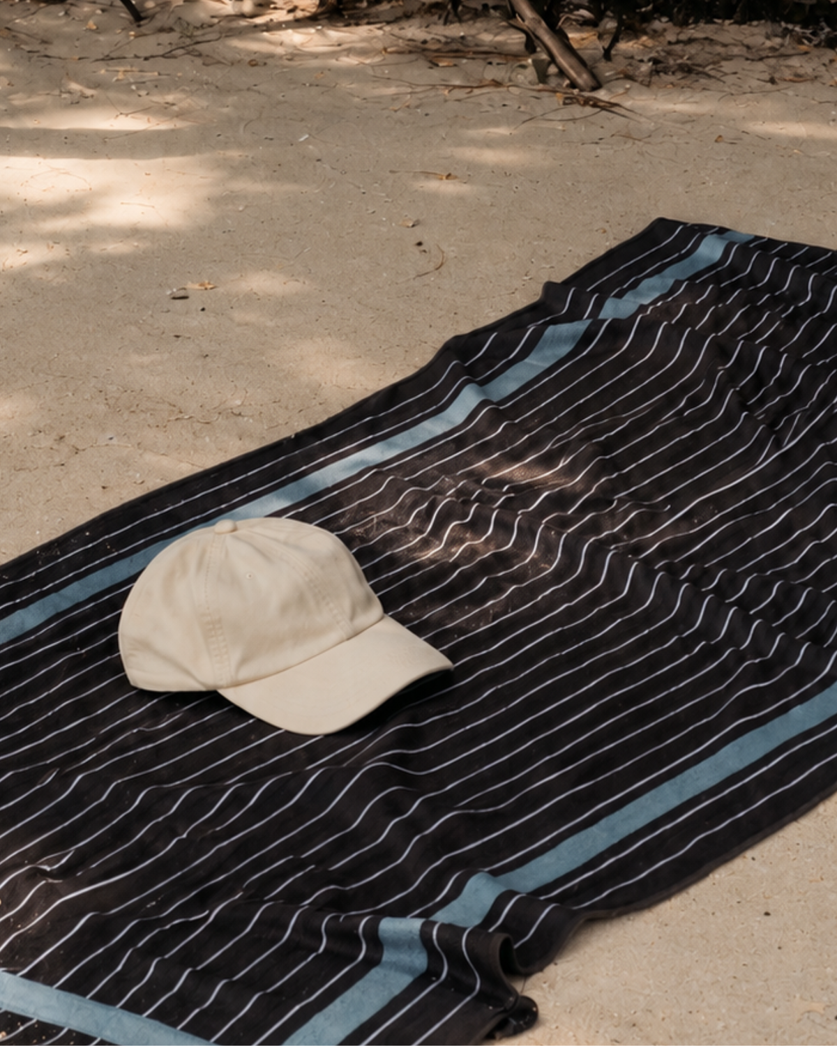 Truffle sand free beach towel laid on the sand, chocolate brown with fine pinstripes and a pale blue border, with a cream cap on top